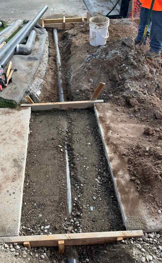 Contractor installing drainage pipe in a trench as part of a permit for curb drain project before concrete restoration.