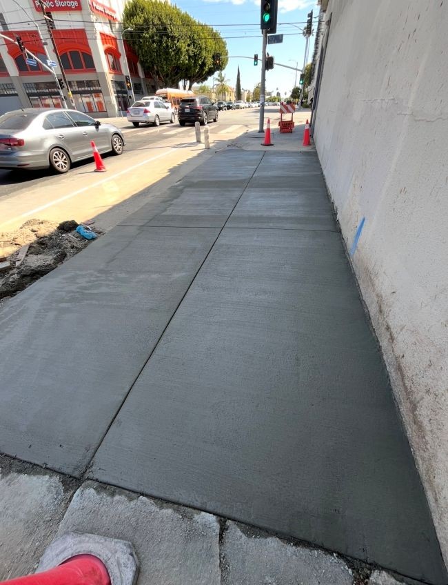 Freshly poured residential concrete sidewalk completed under a permit for sidewalk repair, secured with safety cones and caution tape.