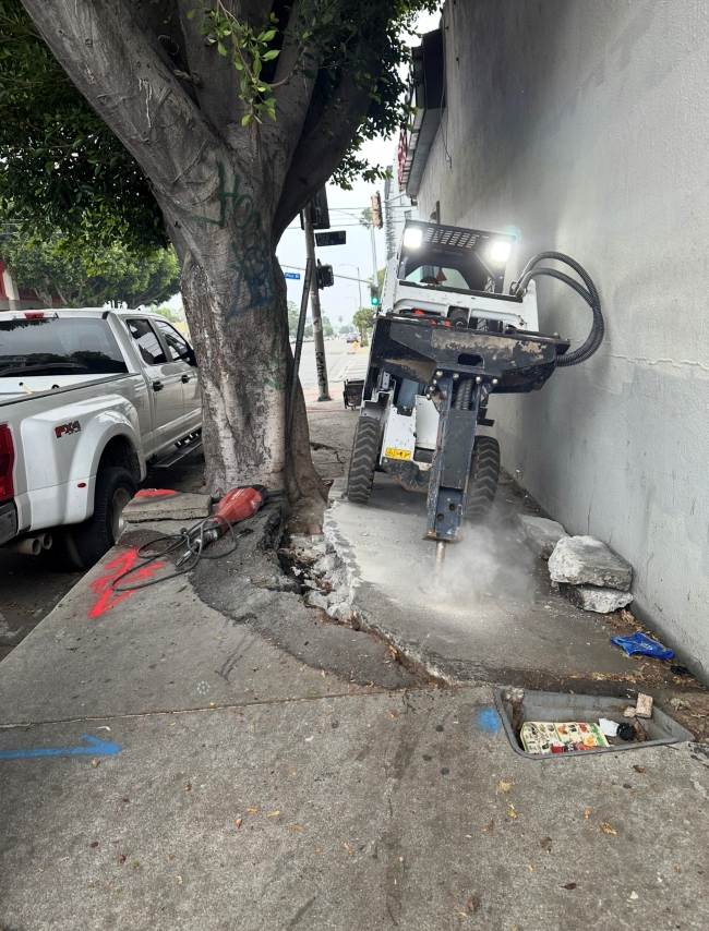 Hydraulic breaker removing damaged concrete sidewalk under a permit for sidewalk repair to prepare for sidewalk reconstruction.