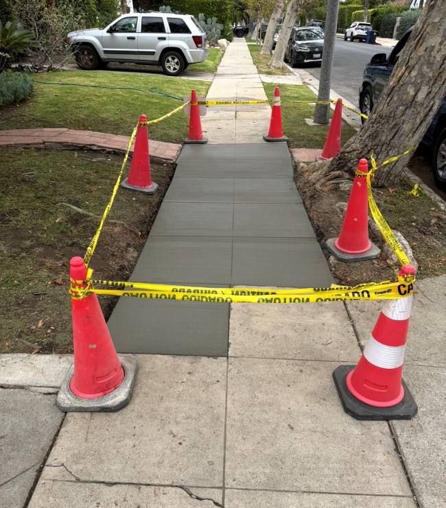 Freshly poured residential concrete sidewalk completed under a-permit-for-sidewalk-repair, secured with safety cones and caution tape.