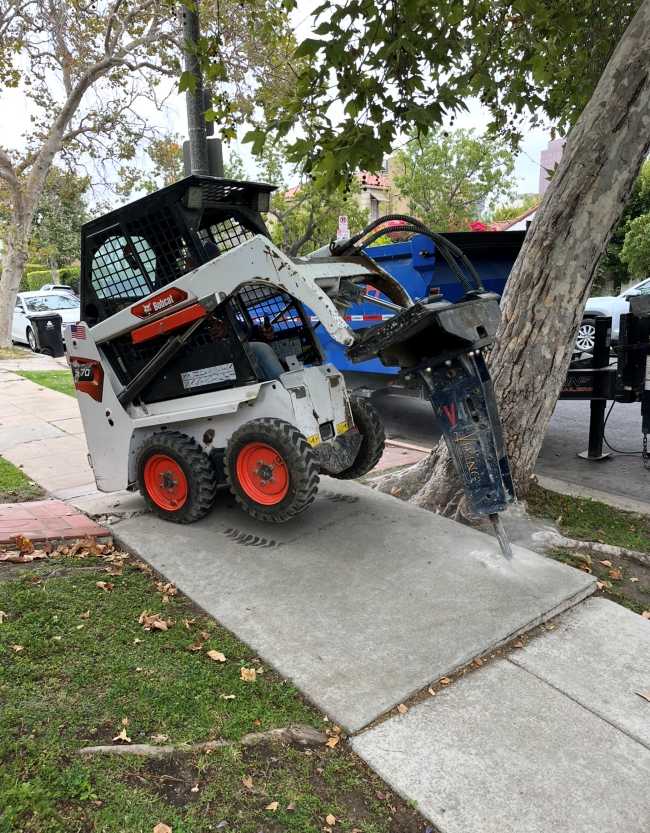 Sidewalk demolition using a skid steer and hydraulic breaker after receiving permit for sidewalk repair for concrete replacemen