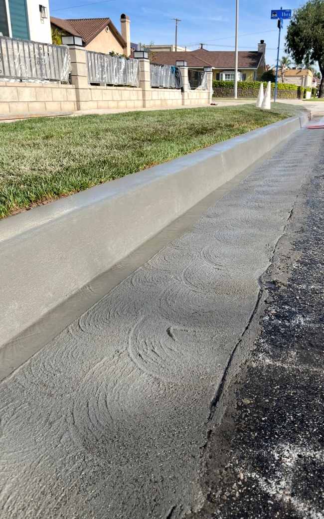 Close-up of a newly constructed concrete curb and gutter with smooth finish beside a residential roadway and grass parkway.