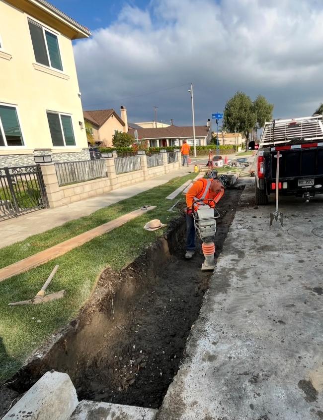 Construction worker compacting the trench during residential curb and gutter installation before new concrete is poured.